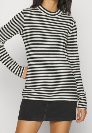 Sort-hvid stribet langærmet top med høj hals, kombineret med en sort denimskørt. Stoffet ser blødt og tætsiddende ud.
