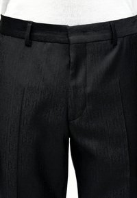 Pantalon noir taille haute avec un motif texturé subtil, passants de ceinture, et une couture centrale sur la ceinture avant.