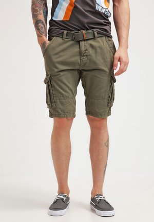 Man draagt olijfgroene cargoshorts met meerdere zakken, een zwarte riem, een donker T-shirt met print en grijze veterschoenen.