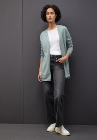 Dlouhý cardigan mentolové barvy přes bílý tričko, spárovaný s černými kalhotami širokého střihu a světlými teniskami. Jednoduchý design a jemná textura.