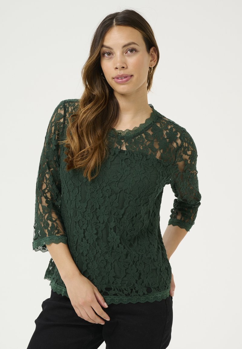 Blusa verde in pizzo con maniche a tre quarti, scollatura e orlo ondulati, caratterizzata da intricate fantasie floreali e una finitura texturizzata.