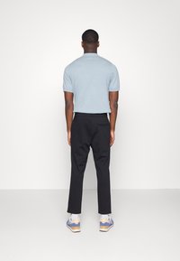 Lichtblauwe polo met korte mouwen, gecombineerd met zwarte broek. De outfit wordt aangevuld met casual multikleurige sneakers met witte accenten.