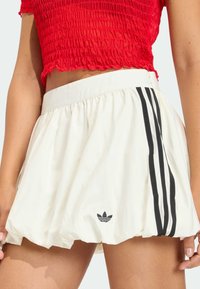 Bijela sportska suknja s crnim bočnim prugama i izvezenim logom. Prozračan dizajn s naboranim strukom. Teksturirana tkanina.