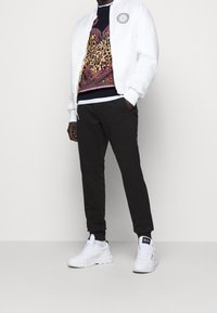 Vit bomberjacka, mönstrad tröja med djurmotiv, svarta sweatpants och vita sneakers. Har logotyp på jackan och tröjan.