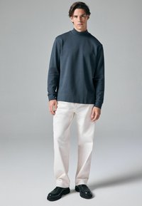 Marineblå langærmet turtleneck, tykk bomuldsmateriale, afslappet pasform. Kombineret med hvide lige ben bukser og sorte snørebåndssko.