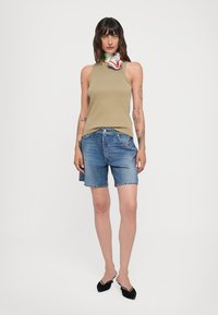 Khaki bez piedurknēm tops, apvienots ar ziliem džinsiem šortiem. Tops ir gluds, bet šorti ir ar izplēstu apakšmalu. Melni plakani apavi noslēdz tērpu.