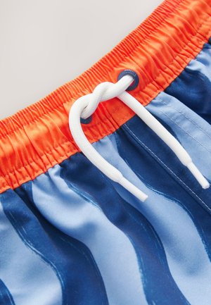 Costume da bagno con motivo ondulato blu e bianco, vita elastica arancione con coulisse bianca e dettagli con occhielli.