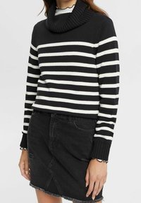 Schwarz-weißer gestreifter Strickpulli mit Wasserfallkragen, ausgestattet mit langen Ärmeln und gerippter Textur. Kombiniert mit einem verwaschenen schwarzen Jeansrock.