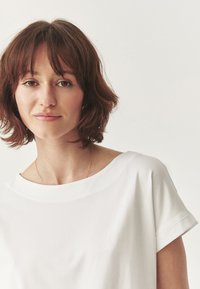 White cotton t-shirt with a relaxed fit, wide neckline, and short rolled sleeves. Smooth fabric texture, minimal design, no patterns or accents.