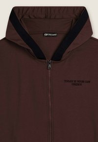 Veste à capuche zippée marron avec des bordures noires à l'intérieur de la capuche, étiquette de marque "FREDDY" au col, et "AUJOURD'HUI EST VOTRE JOUR FREDDY" brodé sur la poitrine.