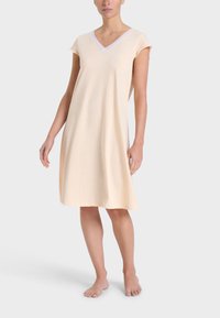 Camisone corto color pesca chiaro con scollatura a V e maniche corte. Realizzato in tessuto morbido, presenta un bordo bianco a contrasto lungo il colletto.