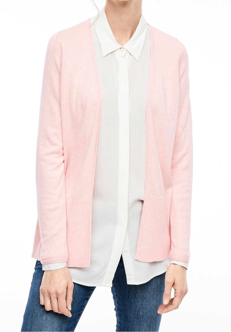 Femme portant un cardigan rose clair ouvert sur une chemise blanche boutonnée et un jean bleu, montré du cou aux hanches.