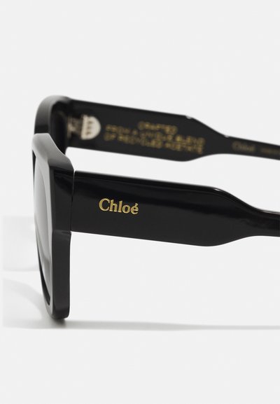 Mustad mustast atsetaadist päikeseprillid, millel on julge ruudu kuju. Sinne kõrvale on kuldsete tähtedega kirjutatud brändi nimi "Chloé".