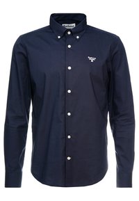 Laivastonsininen pitkähiha-särkkään puuvillasta valmistettu paita, jossa on kauluksessa napillinen kaulus, valkoiset napit ja pieni kirjailtu logo rinnassa.