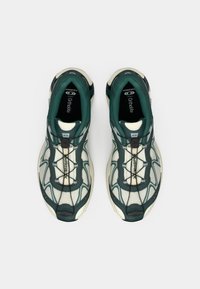 Πράσινα και εκρού αθλητικά παπούτσια με πλεκτό επάνω μέρος, περίπλοκο σύστημα κορδονιών και ενισχυμένη σόλα, σχεδιασμένα για άνεση και απόδοση.