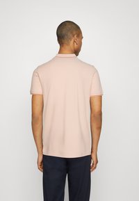 Helles rosa Polohemd mit kurzen Ärmeln, kontrastierendem Kragen und Ärmelsäumen sowie einer sauberen, glatten Stoffoberfläche.