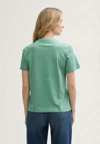 T-shirt en coton vert menthe à manches courtes avec un col rond, coutures plates et une coupe décontractée, associé à un jean en denim bleu.