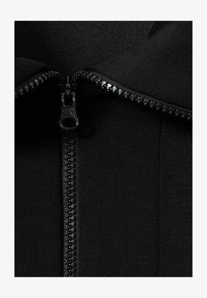Indumento zip nero con una texture liscia. Presenta una zip centrale con denti in plastica e un tirante, circondata da un colletto ripiegato.