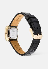 Montre rectangulaire en or avec bracelet en cuir noir, boucle et fond gravé affichant la marque, le numéro de série et les détails du mouvement.