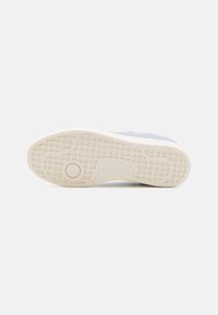 Baskets Lacoste avec tige en daim bleu texturé, semelle en caoutchouc blanche et motif de bande de roulement. Comprend un détail de logo circulaire sur la semelle.