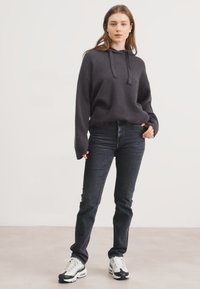 Szara, kapturowa bluza o luźnym kroju, z kieszeniami z przodu, zestawiona z ciemnoniebieskimi dżinsami i masywnymi białymi sneakersami. Gładka tekstura, casualowy design.