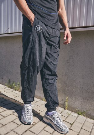 Juoda, lengva kelnaitė su laisvu siluetu ir elastingais kulkšnomis, su apvaliu logotipu kairėje klubo pusėje. Dėvimos su pilkais sportiniais bateliais.