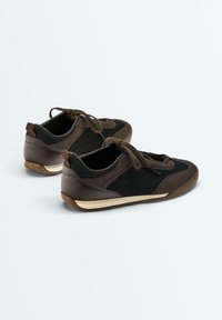 Paire de baskets décontractées marron et noires à lacets, en tissu mesh avec semelles en caoutchouc sur fond clair.