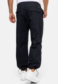 Mørkeblå cargo bukser med elastiske manchetter, der har baglommer og en afslappet pasform, parret med hvide sneakers.