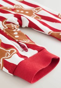 Piros és fehér csíkos anyag, gingerbread ember mintákkal; kis piros cipzárral rendelkezik, és a mandzsettákon puha, rugalmas textúrájú.