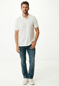 Witte polo met textuurstrepen, korte mouwen, gecombineerd met blauwe jeans en witte sneakers; casual, relaxed fit.