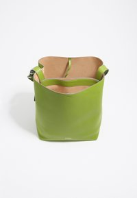 Sac seau en cuir vert avec une bandoulière ajustable, intérieur beige et petit logo de la marque embossé en bas au centre à l'avant.