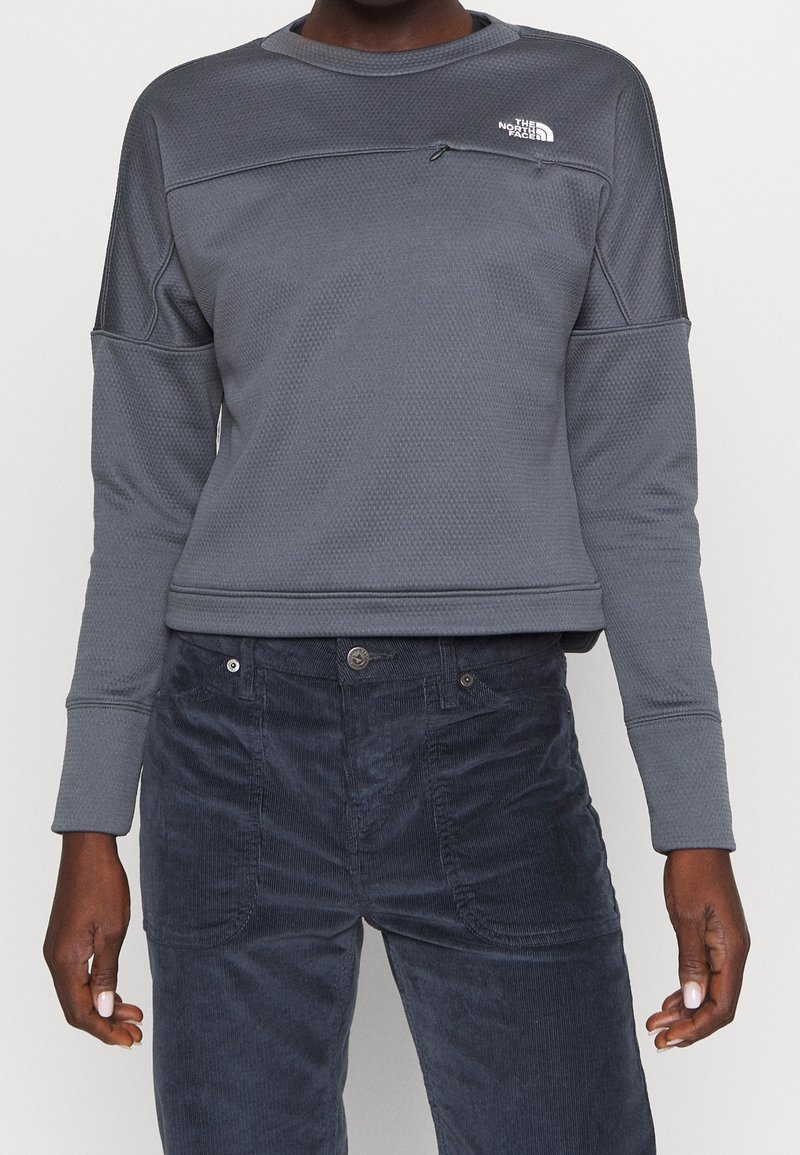 Sweatshirt gris texturé à manches longues et col rond. Présente une couture horizontale et une petite poche zippée sur la poitrine.