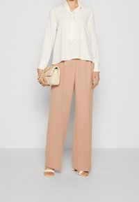 Bílá blůza s krčním vázáním, doplněná vysokými béžovými kalhotami s širokými nohavicemi. Zajímavostí je světle béžová taška s řetízkovým popruhem.