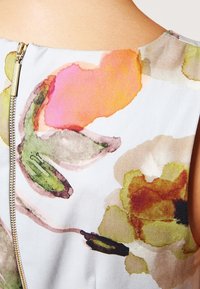 Gros plan sur une robe blanche sans manches avec une fermeture éclair dorée et de grands motifs floraux abstraits en rose, vert et jaune au dos.