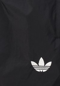 Tissu noir avec logo Adidas trèfle blanc brodé près du coin inférieur droit.
