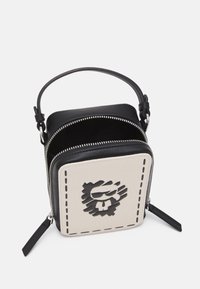 Borsa in pelle nera con pannello beige chiaro che presenta una grafica di un leone nero. Chiusura con zip, tracolla regolabile e finiture testurizzate sui bordi.
