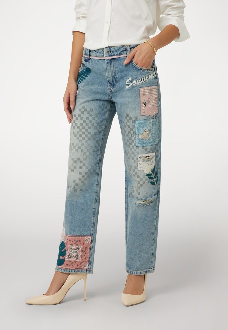 Šviesiai mėlynos džinsinės kelnės su rožinėmis ir mėlynomis aplikacijomis, turinčiomis gėlių ir geometrinių raštų, pažeistą tekstūrą ir tiesų kirpimą.