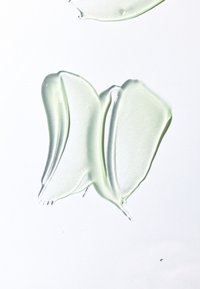 Transparente gelartige Substanz, blassgrün, mit glatter, glänzender Oberfläche; unregelmäßige Formen und dünne Kanten auf weißem Hintergrund.