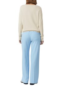 Helles beiges gestricktes Sweatshirt mit einem runden Ausschnitt, kombiniert mit hellblauen weiten Hosen, die eine glatte Textur und eine lockere Passform zeigen.