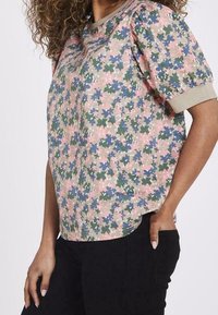 Top de manga corta con estampado floral en tonos rosas, verdes y azules; presenta un escote redondeado y una textura en la tela. Combinado con pantalones negros.