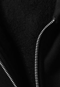 Μαύρο ύφασμα με ανοιχτό μερικώς ασημένιο μεταλλικό φερμουάρ, που δείχνει υφή της εσωτερικής επένδυσης κάτω από το εξωτερικό υλικό.