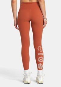 Höga, figurnära leggings i bränd orange stretchtyg. Utrustade med vita grafiska logotyper på vänster ben. Ankellång design.