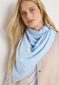 Bufanda suave de color azul claro, hecha de un tejido texturizado, que cae elegantemente alrededor del cuello, combinada con un chaleco de forro polar de color crema.