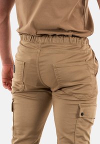Khaki cargobroek met elastische tailleband, grote zijzakken en gestikt detail. Zachte stof met een gladde textuur.