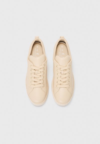 Baskets en cuir beige avec bout rond, lacets à l'avant, col rembourré, et semelle texturée. Marque visible sur les semelles intérieures.