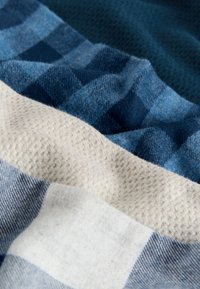 Tekstiilid erinevates sinise, kreemja ja valge tooni varjundites; sisaldab ruudulist mustrit ja tekstuurseid pindu kontrastse siledama alaga.
