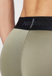 Nike Pro träningsleggings i olivgrön, med ett svart elastiskt midjeband med "NIKE PRO"-logga och flatlock-sömnadsdetalj.