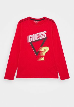 Rød langærmet skjorte med "GUESS" i hvid, en stor sort trekant og et gult spørgsmålstegn på forsiden.
