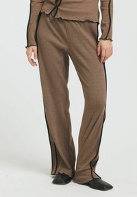 Braune gerippte Hose mit lockerer Passform, die schwarze Seitenstreifen und dekorative gewellte Kanten an der Taille und dem Saum aufweist. Glatte Textur.