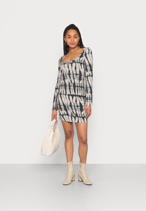 Vestido justo com mangas longas, padrão tie-dye em preto e creme, decote redondo e detalhe em fenda. Combinado com uma mala bege e botas de salto.